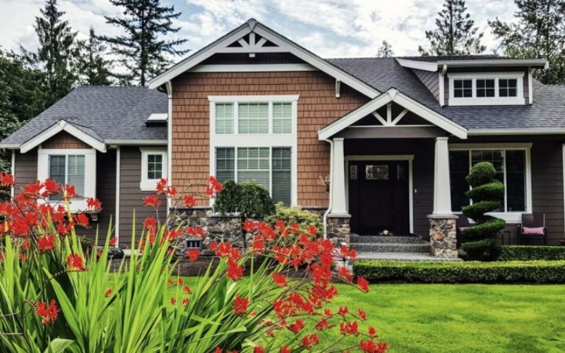 nice house with trees in back and red flowers in front