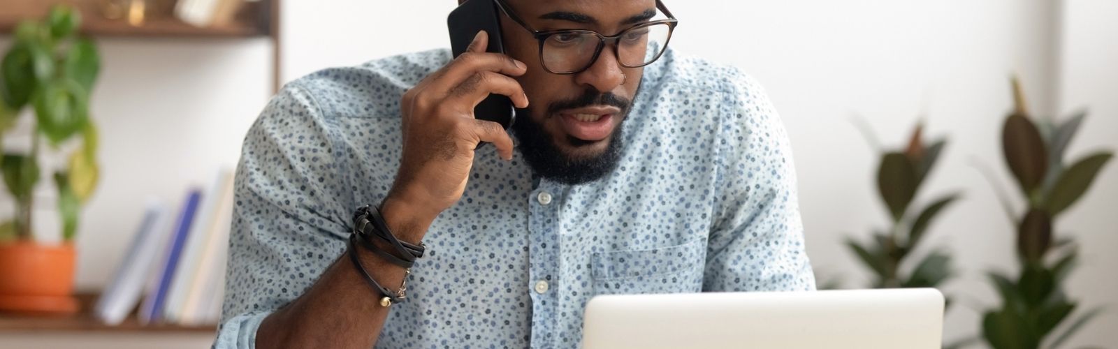 man talking on phone while researching on laptop computer