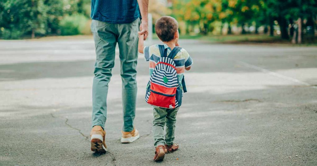 father walking son wearing a backpack to school