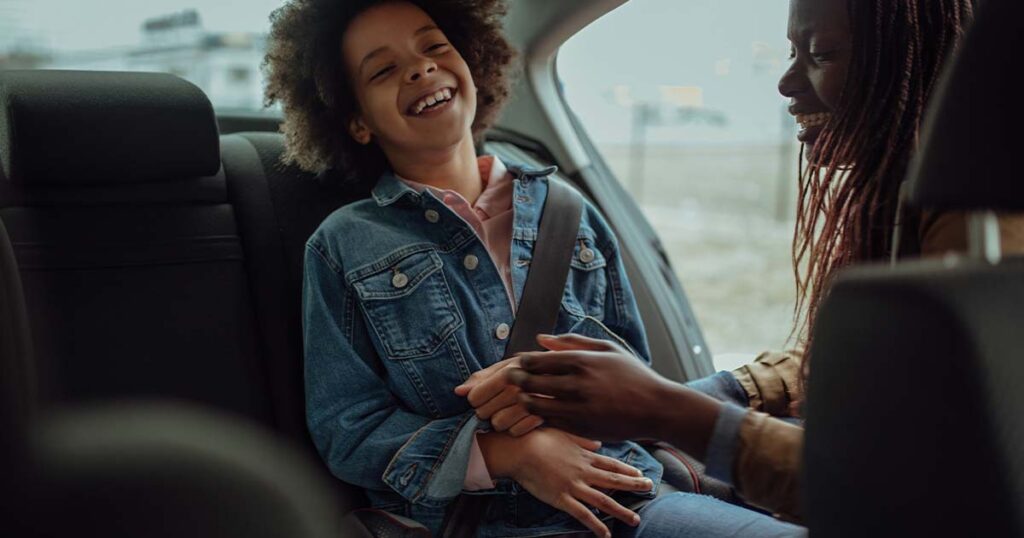 mother buckling kid's seatbelt in back seat