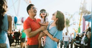 A cute mixed race family enjoys the rides and sun at the fair activities on Santa Monica Pier in Los Angeles, California. They all wear sunglasses with big smiles.