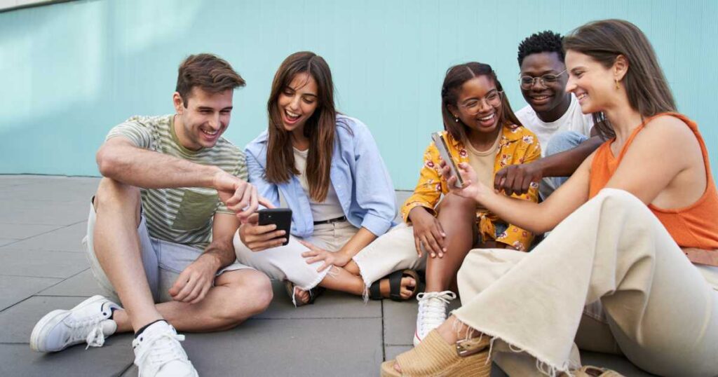 Group of students using mobiles app outdoors and smiling sitting in a floor checking cell phone multimedia or social media.