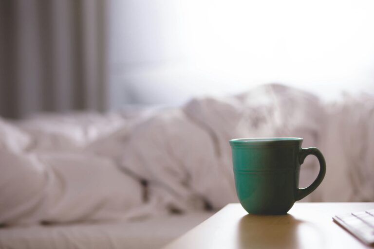 A hot beverage in a green mug with white sheets in background