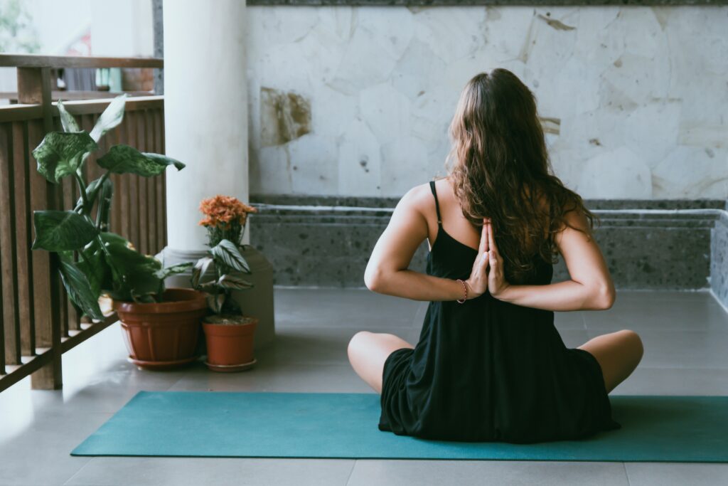 A woman facing away from us, sitting on a mat in a yoga pose