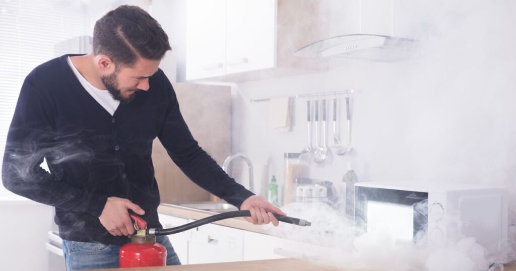 man using fire extinguisher in kitchen with smoke and microwave